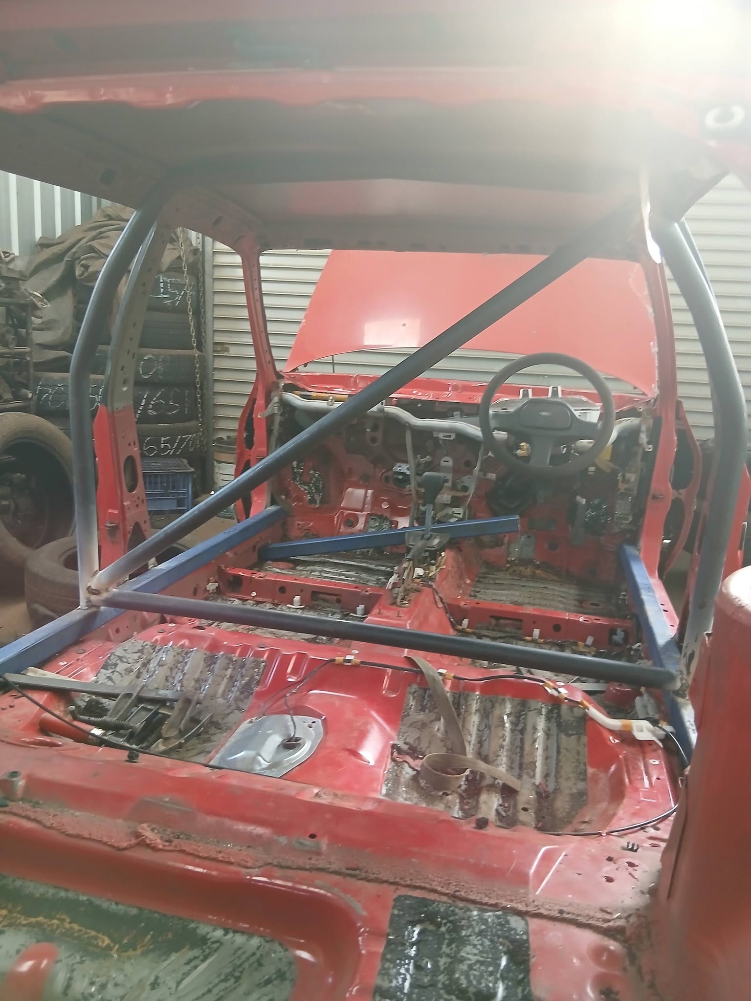 Interior of a red car shell fitted with roll cage bars in a workshop